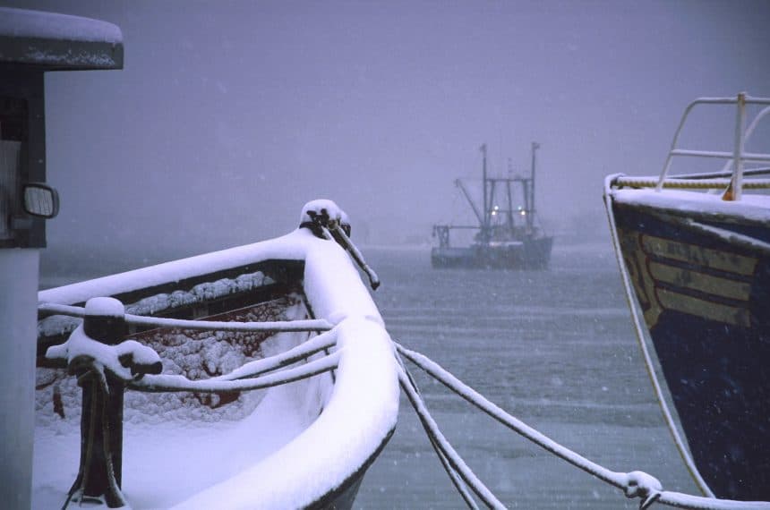 Snow-covered fishing vessels in port during winter, commercial fishing industry scene.