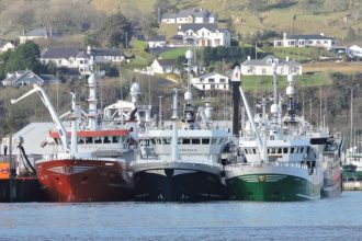 Fishing vessels docked at port in a commercial fishing industry setting with coastal homes in the背景.