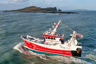 Commercial fishing vessel navigating coastal waters, focus on gear and industry equipment, February.