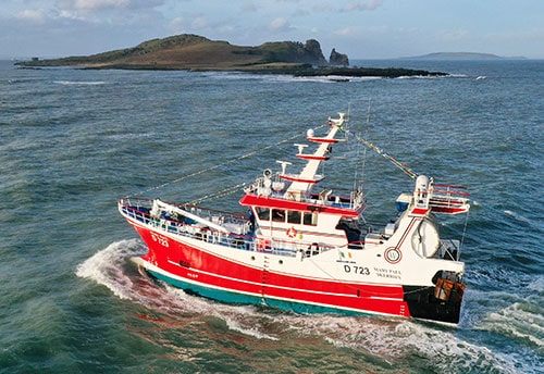 Commercial fishing vessel navigating coastal waters, focus on gear and industry equipment, February.