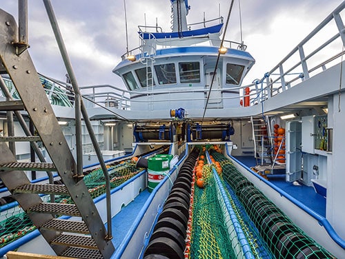 Commercial fishing vessel deck with gear and industry equipment in port setting.