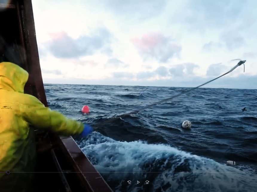 Fishing vessel at sea with crew member and fishing gear in rough waters, commercial fishing industry.