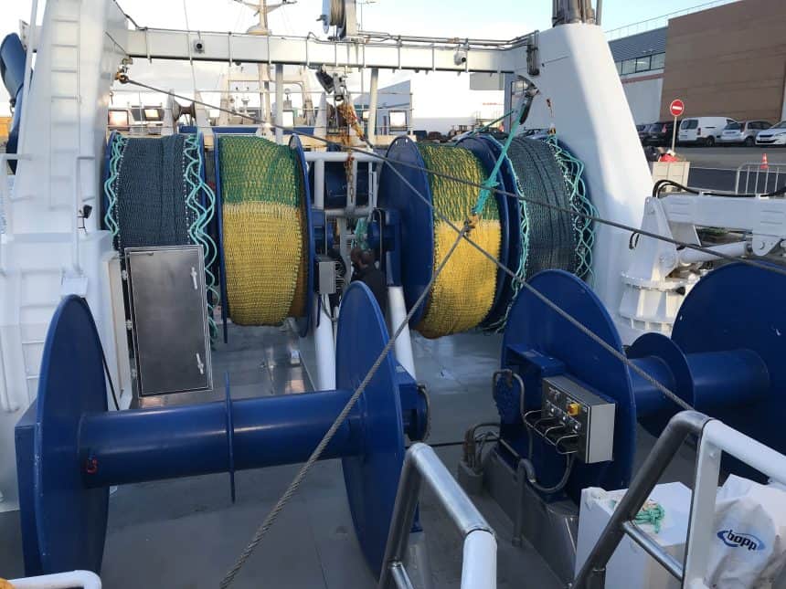 Fishing vessel deck with trawl gear, winches, and industry equipment at port for commercial fishing.