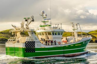 Commercial fishing vessel with green and white hull navigating coastal waters with industry gear on.