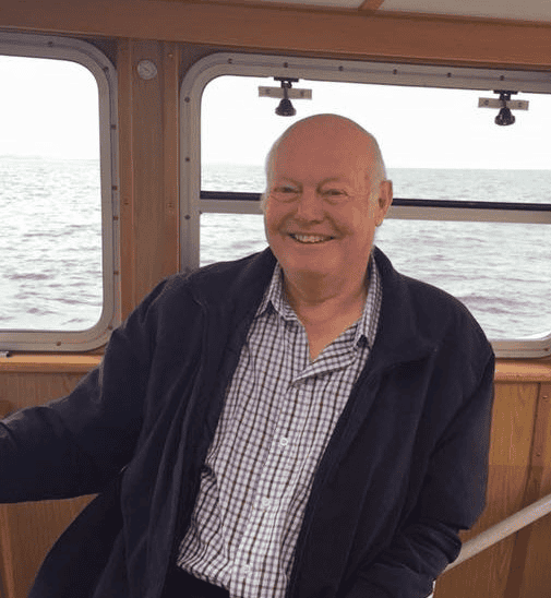 Fisherman smiling on fishing vessel with gear and ocean background in commercial fishing industry.