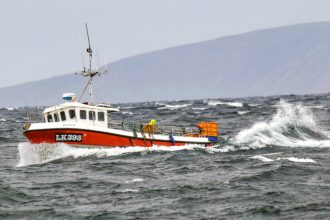 Fishing vessel navigating rough seas in a commercial fishing industry setting with crew onboard.