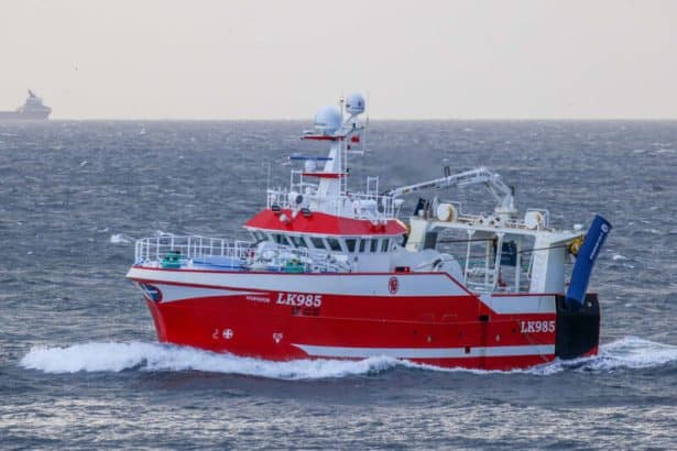 Red fishing vessel LK985 navigating open sea in commercial fishing industry context.