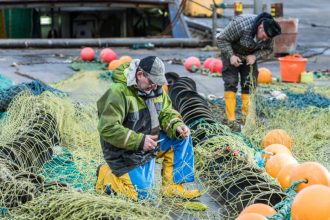 Fishermen repairing fishing gear on a commercial fishing vessel in port, industry equipment, and net.