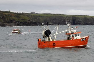 Fishing vessel in rough seas with port cliffs in background, commercial fishing industry publication.