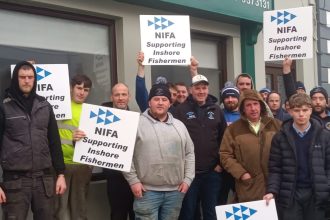 Group of fishermen holding NIFA signs supporting inshore fishermen outside a building in Ireland.