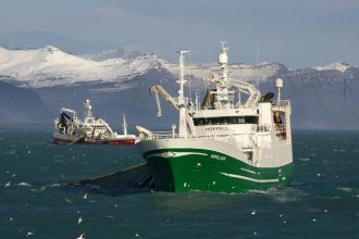 Commercial fishing vessel in icy waters with snow-capped mountains in background, industry gear on a.