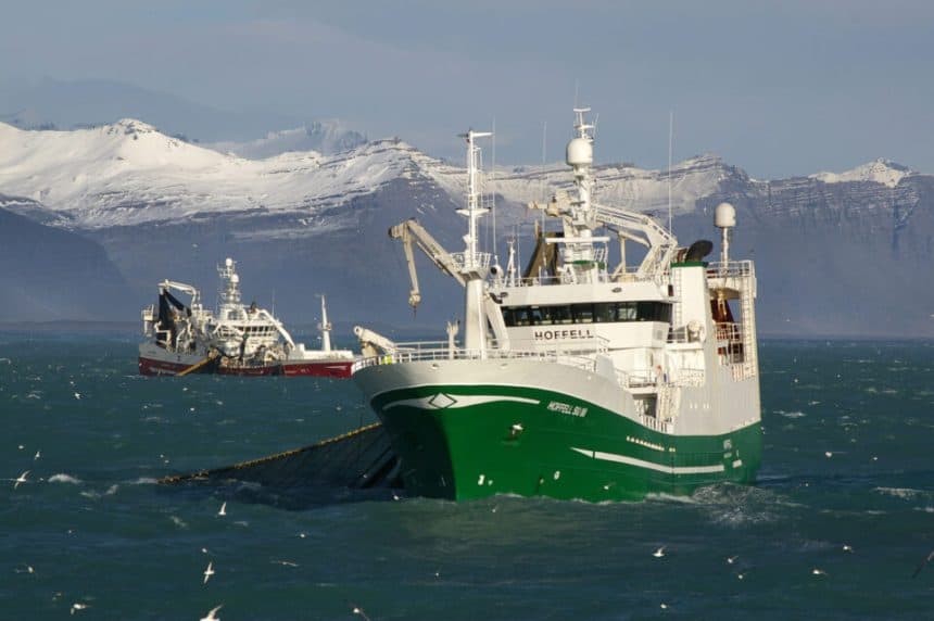 Commercial fishing vessel in icy waters with snow-capped mountains in background, industry gear on a.