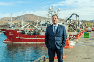 Fishing vessels docked at port with industry equipment and a man in a suit in foreground.