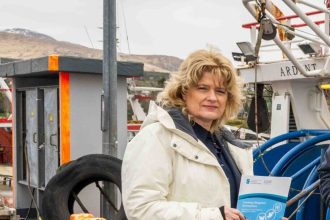 Fisherwoman at fishing vessel port with industry gear and equipment in the background.