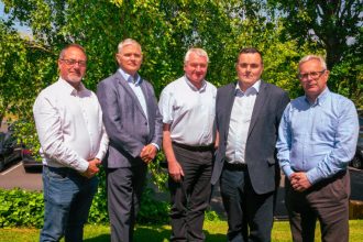 Group of fishermen in suits outdoors, industry event, green trees background.