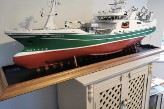 Commercial fishing vessel model with gear and industry equipment on display in a maritime setting.
