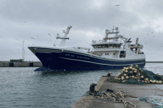 Large fishing vessel docked at port, commercial fishing industry scene, industry equipment visible.
