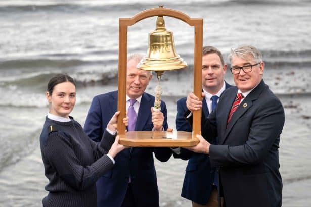 Fishermen and industry officials hold a bell at the shoreline, celebrating a maritime event in the.
