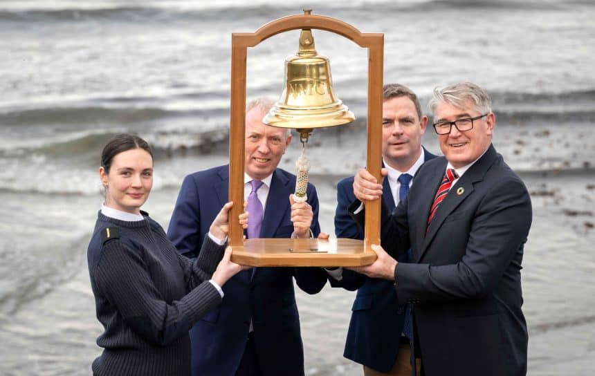 Fishermen and industry officials hold a bell at the shoreline, celebrating a maritime event in the.