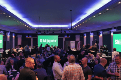 Indoor event with fishing industry professionals, screens display 'The Skipper' branding, industry-­.