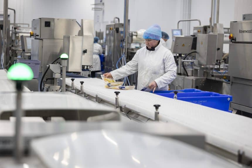 Fishermen working in seafood processing plant with industrial equipment and conveyor belts in the UK.