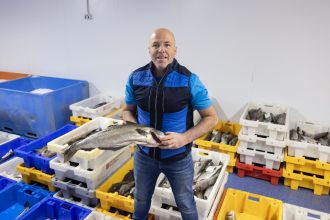 Fisherman holding a large fish in a seafood processing facility with industry crates and equipment.