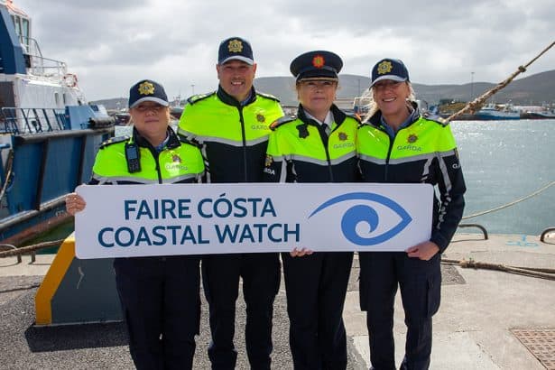 Four fishermen women in high-visibility jackets hold a coastal watch sign at the port with fishing V.