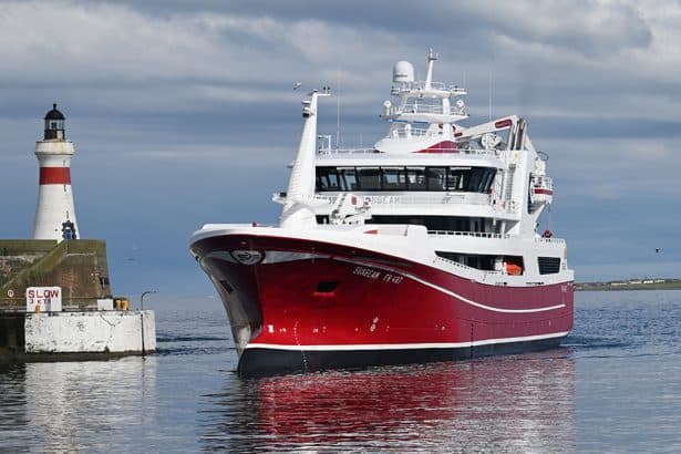 Luxury red and white yacht sailing near a lighthouse in calm waters.