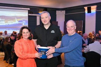 Three people at the Scottish Skipper Expo, holding a support bucket, smiling.