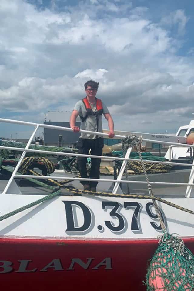 Young fisherman standing on a boat with a cloudy sky background.