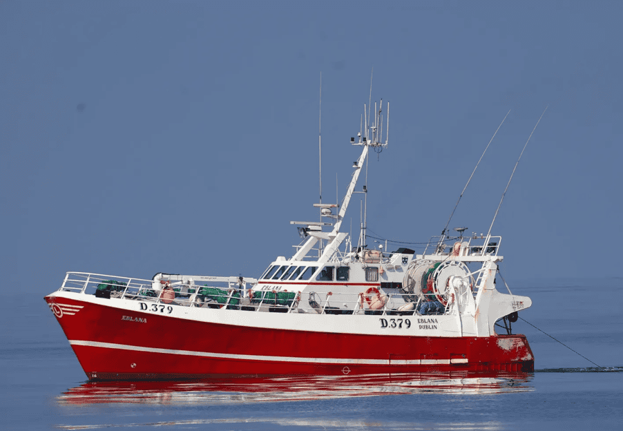Fishing boat with red hull sailing on calm sea under clear sky.