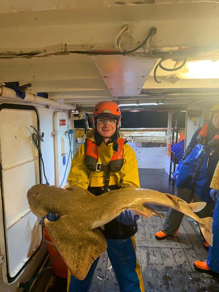 Fisherman holding a large flatfish on a boat deck in Ireland.