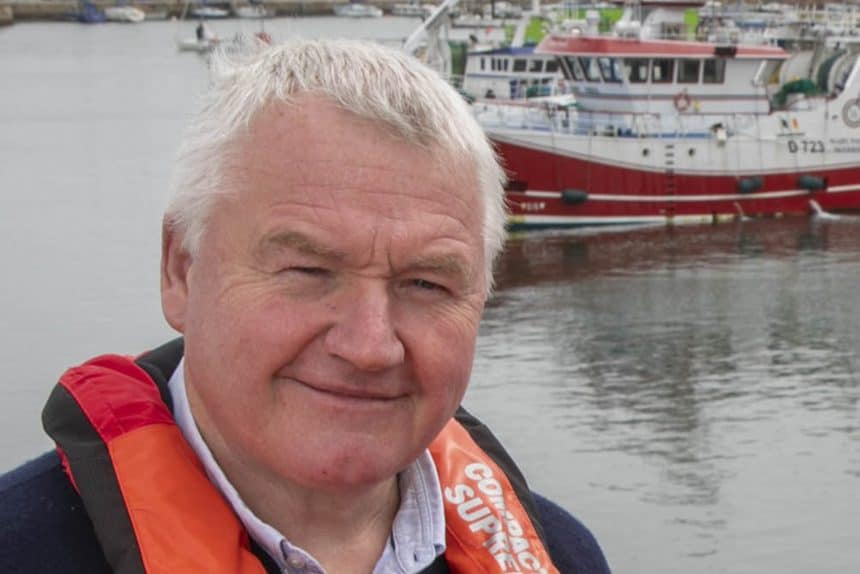 Fisherman in life jacket near boats at a harbor in Ireland.