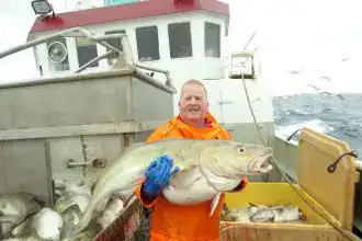 Fisherman holding a large fish on a boat during a fishing trip.
