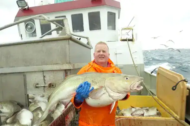 Fisherman holding a large fish on a boat during a fishing trip.
