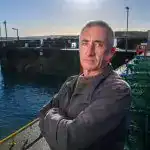 Man standing on dock with fishing boats and crates in background at The Skipper.