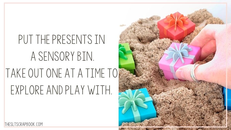 Picture of some of the colourful presents inside a sensory bin filled with kinetic sand. The text reads "put the presents in a sensory bin. Take out one at a time to play with".