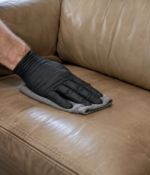 Professional hand cleaning a leather sofa with a cloth for deep stain removal.