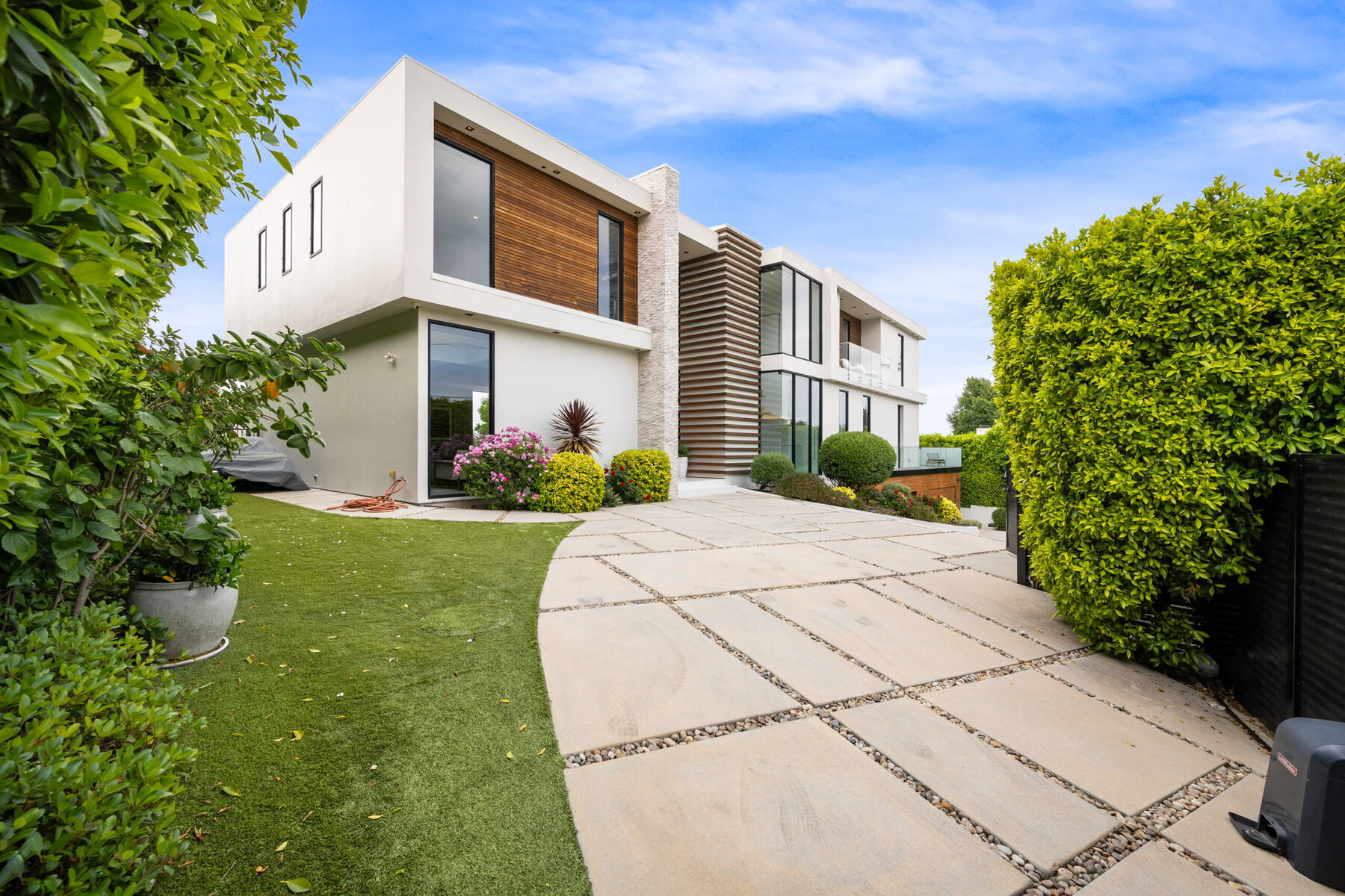 Modern white house with wood accents, green lawn, and stone driveway under blue sky.