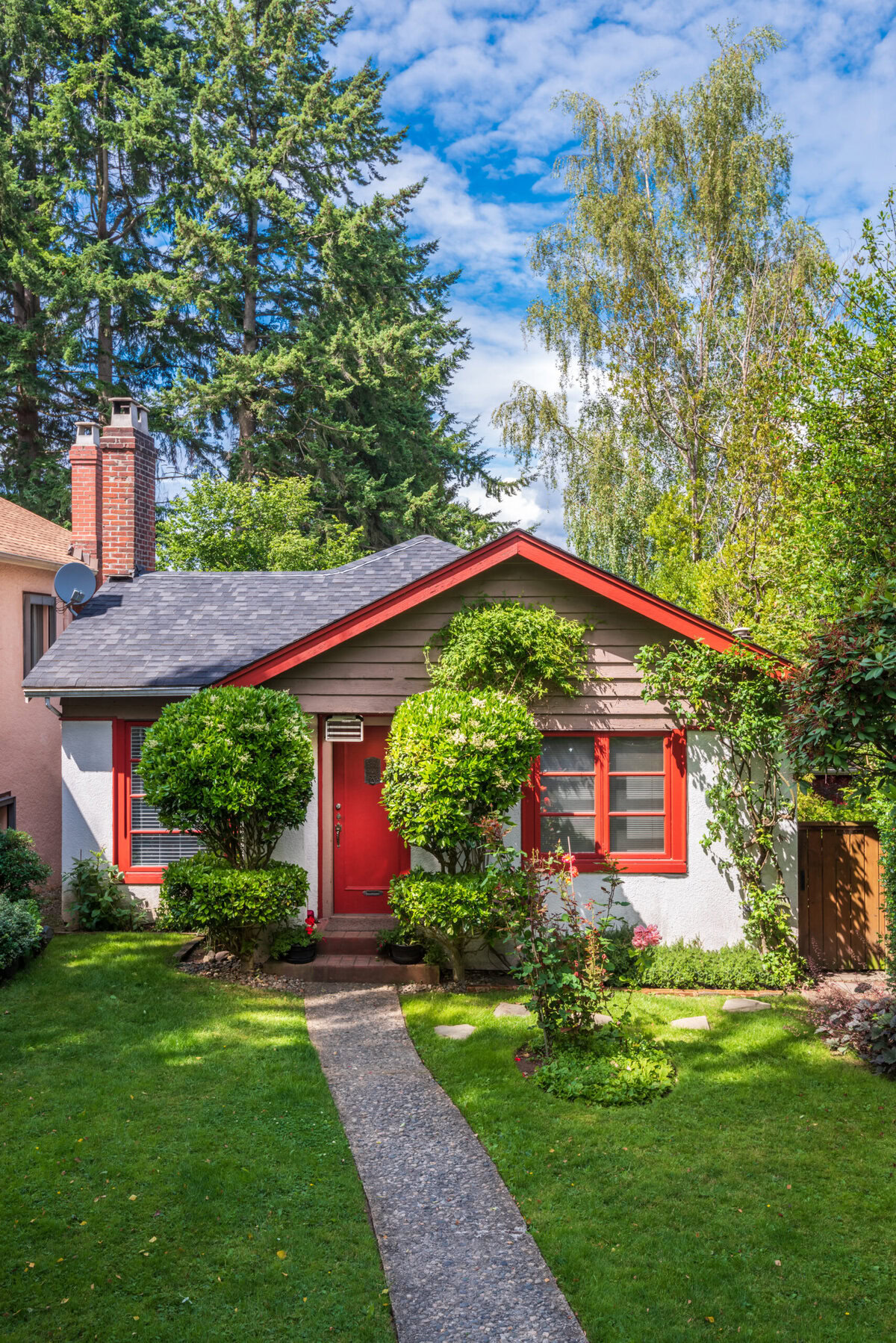 Small house with red door and windows, green lawn, and lush trees