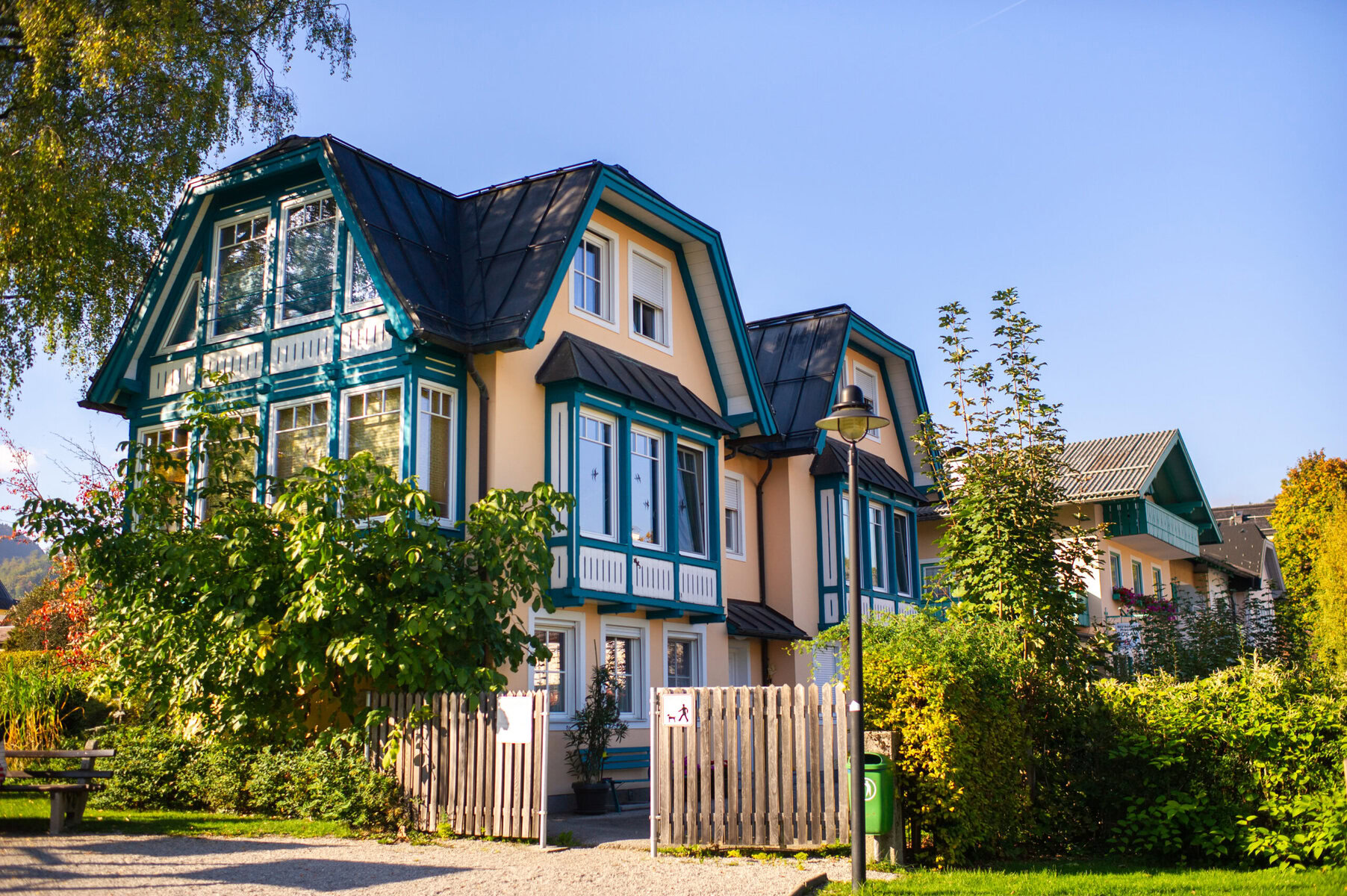Two large, beige houses with dark roofs and teal trim under a clear sky.