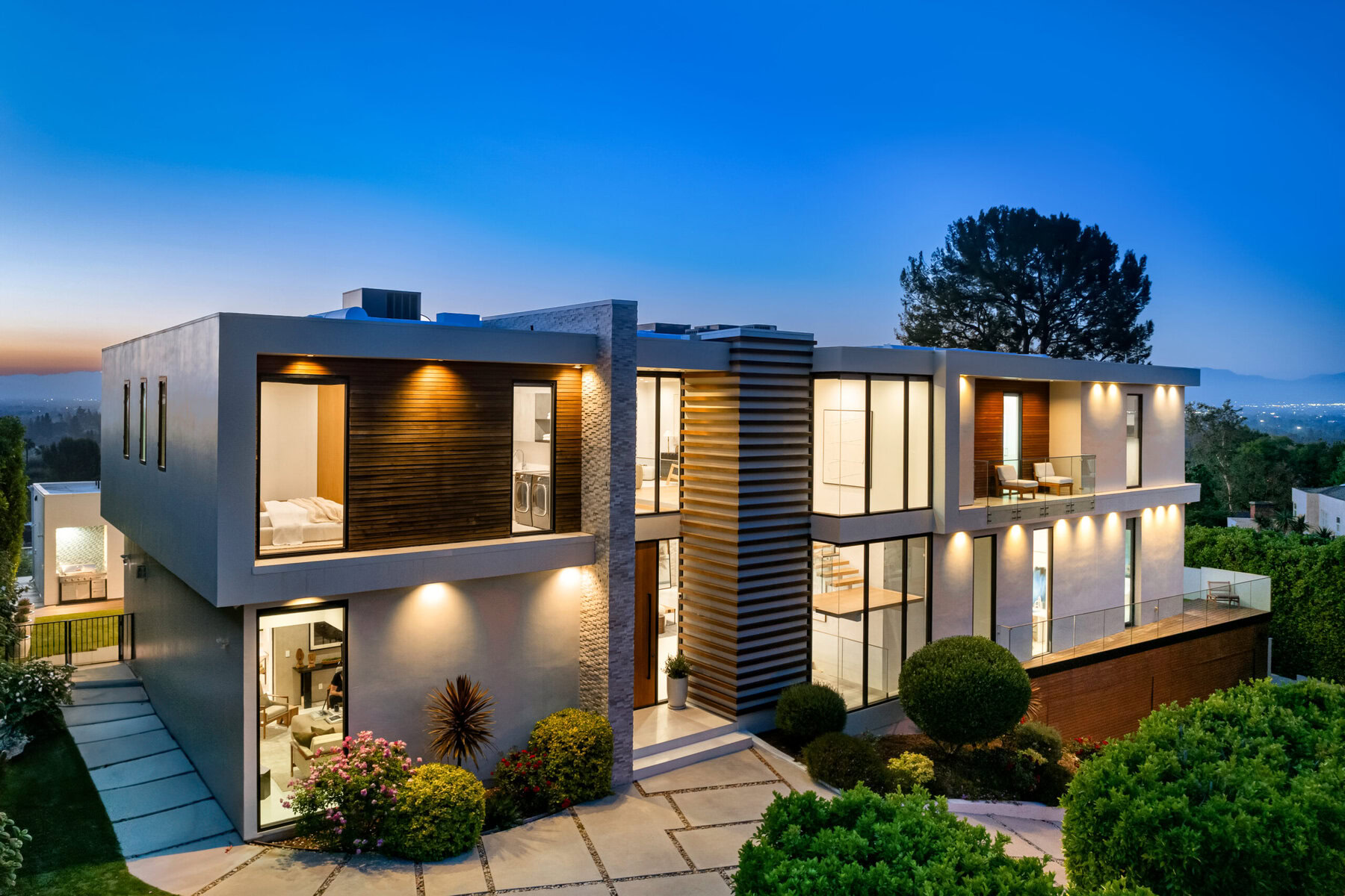 Modern multi-story house with large windows and outdoor lighting at dusk.