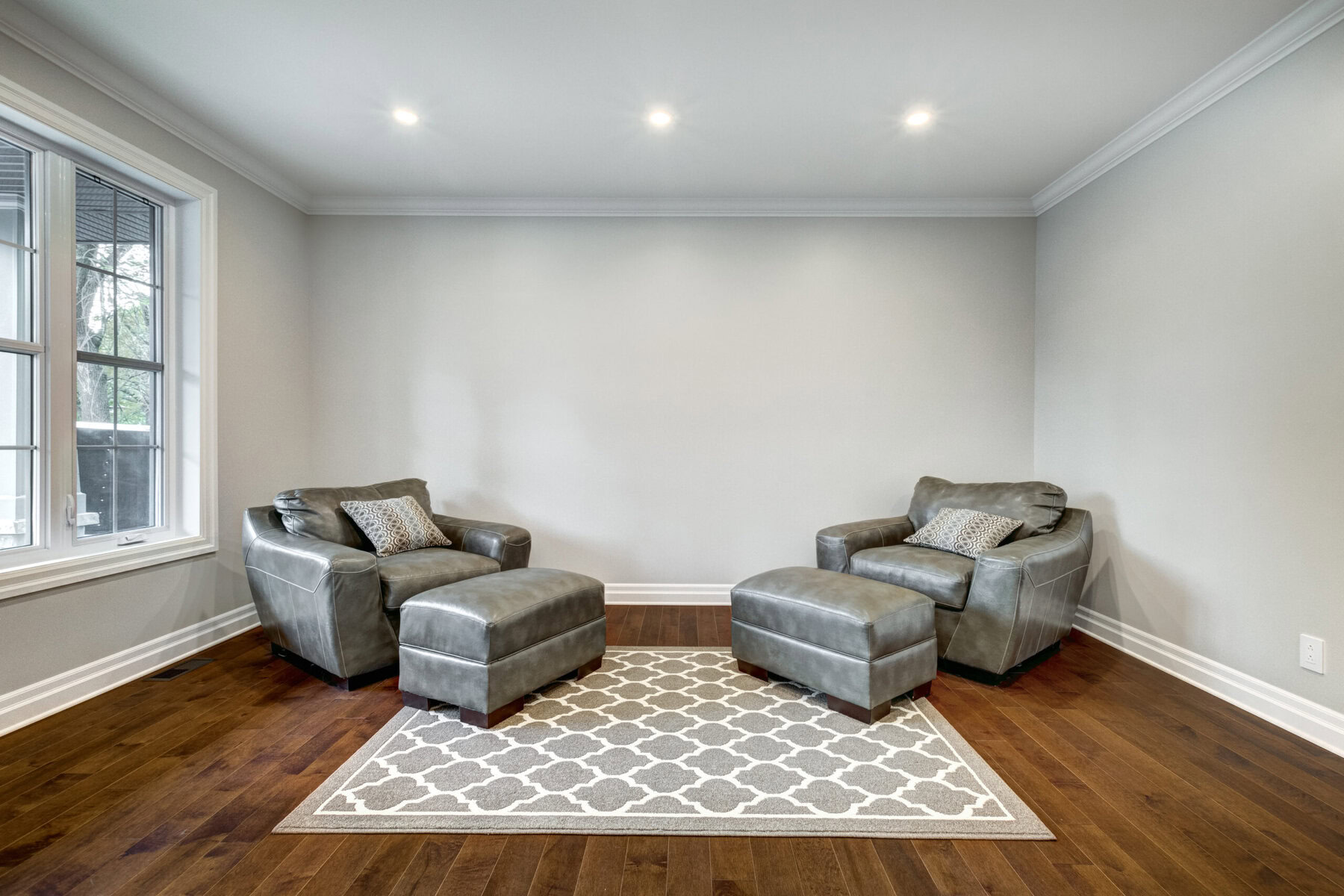 Two grey armchairs and ottomans on a patterned rug in a room.