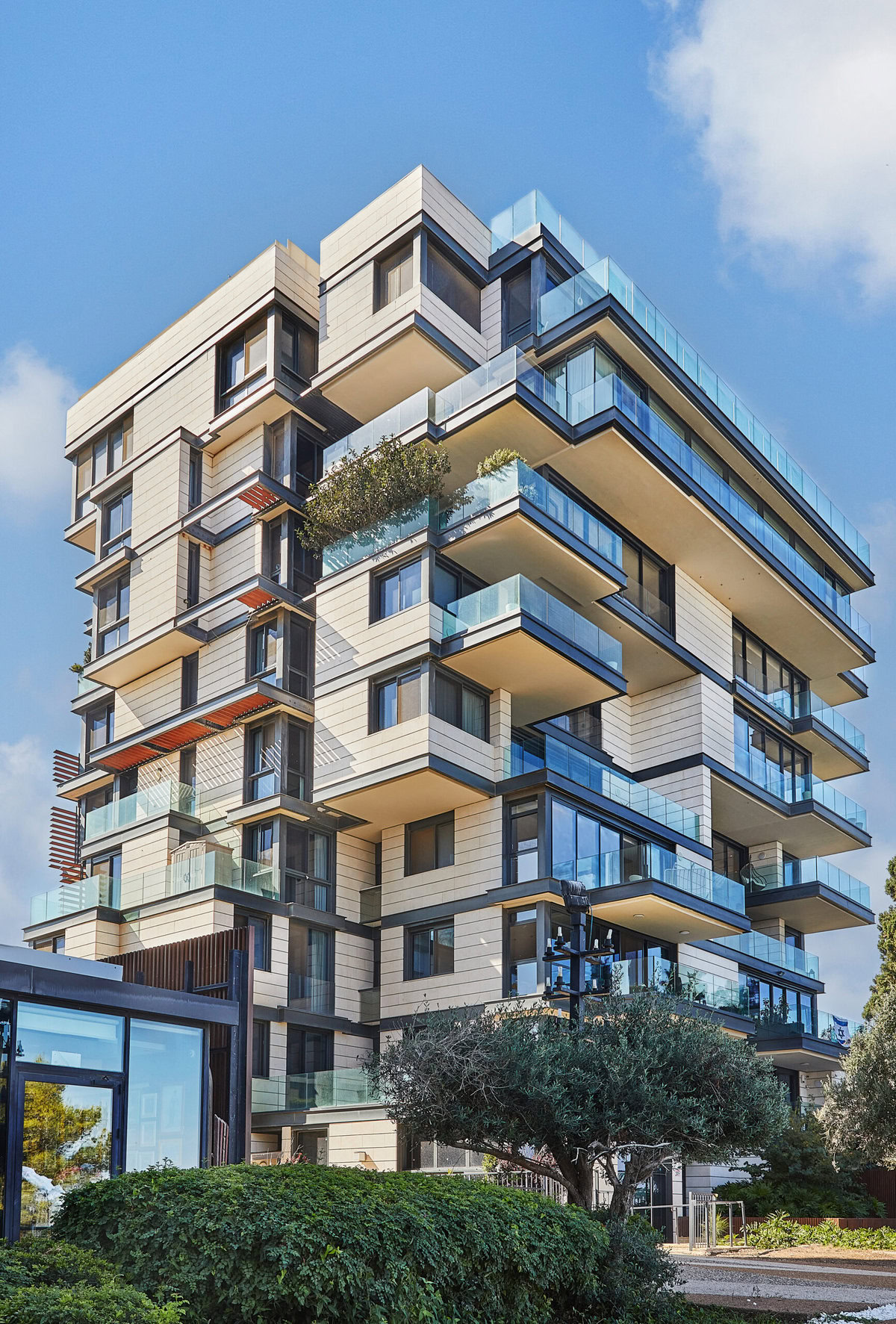 Modern residential building with glass balconies and light-colored facade under blue sky.