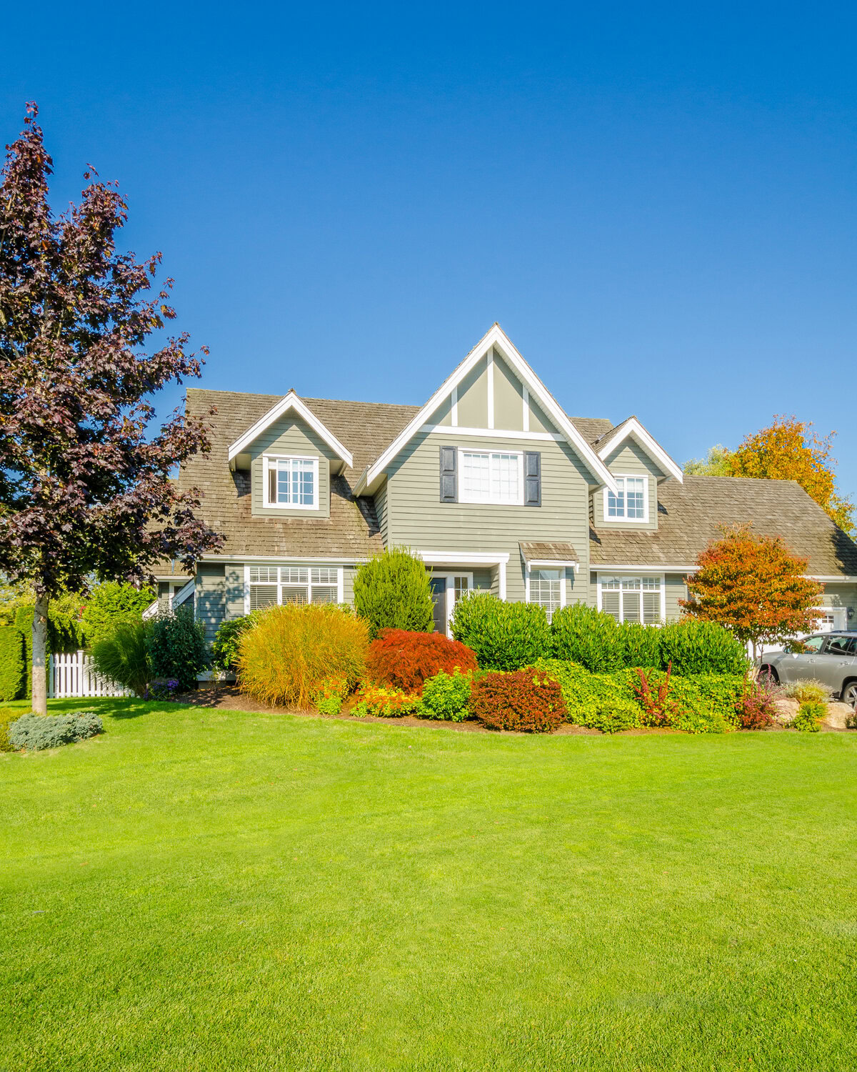 Large green house with white trim, green lawn, and colorful landscaping.