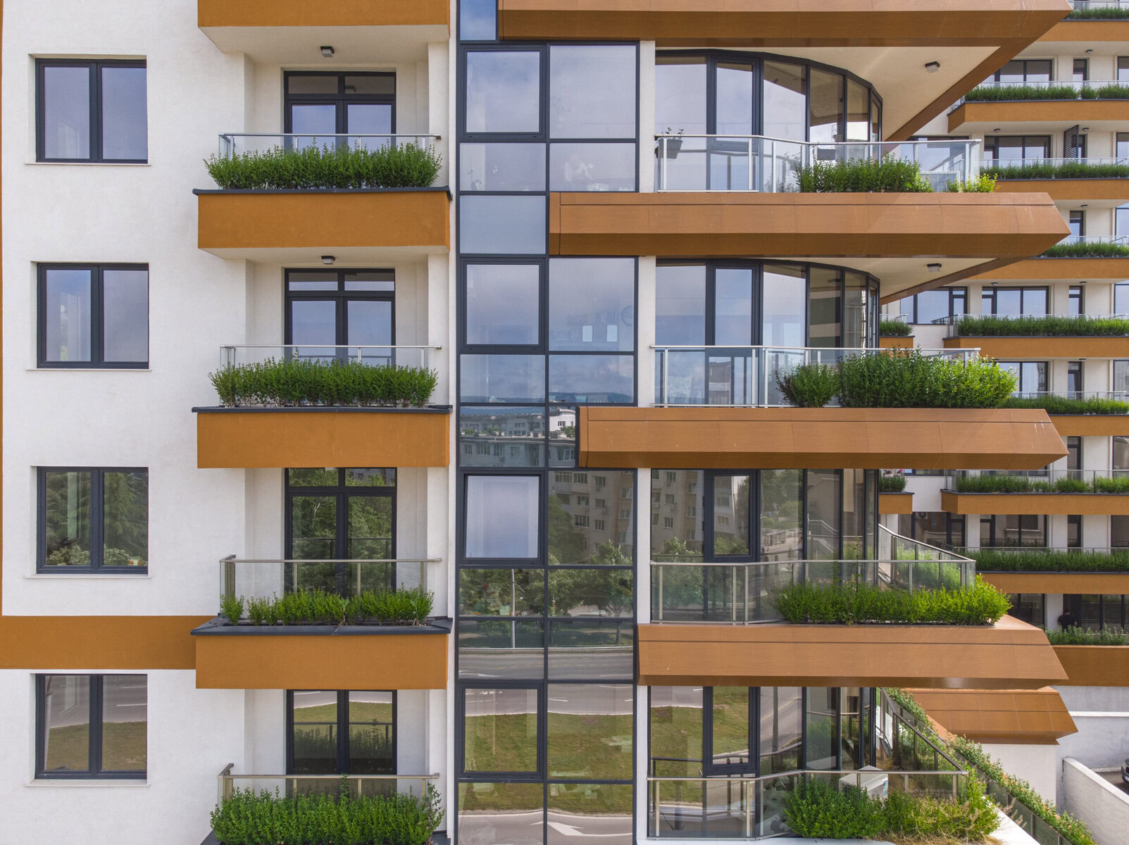 Modern building with white facade, brown balconies, large windows, and green plants.