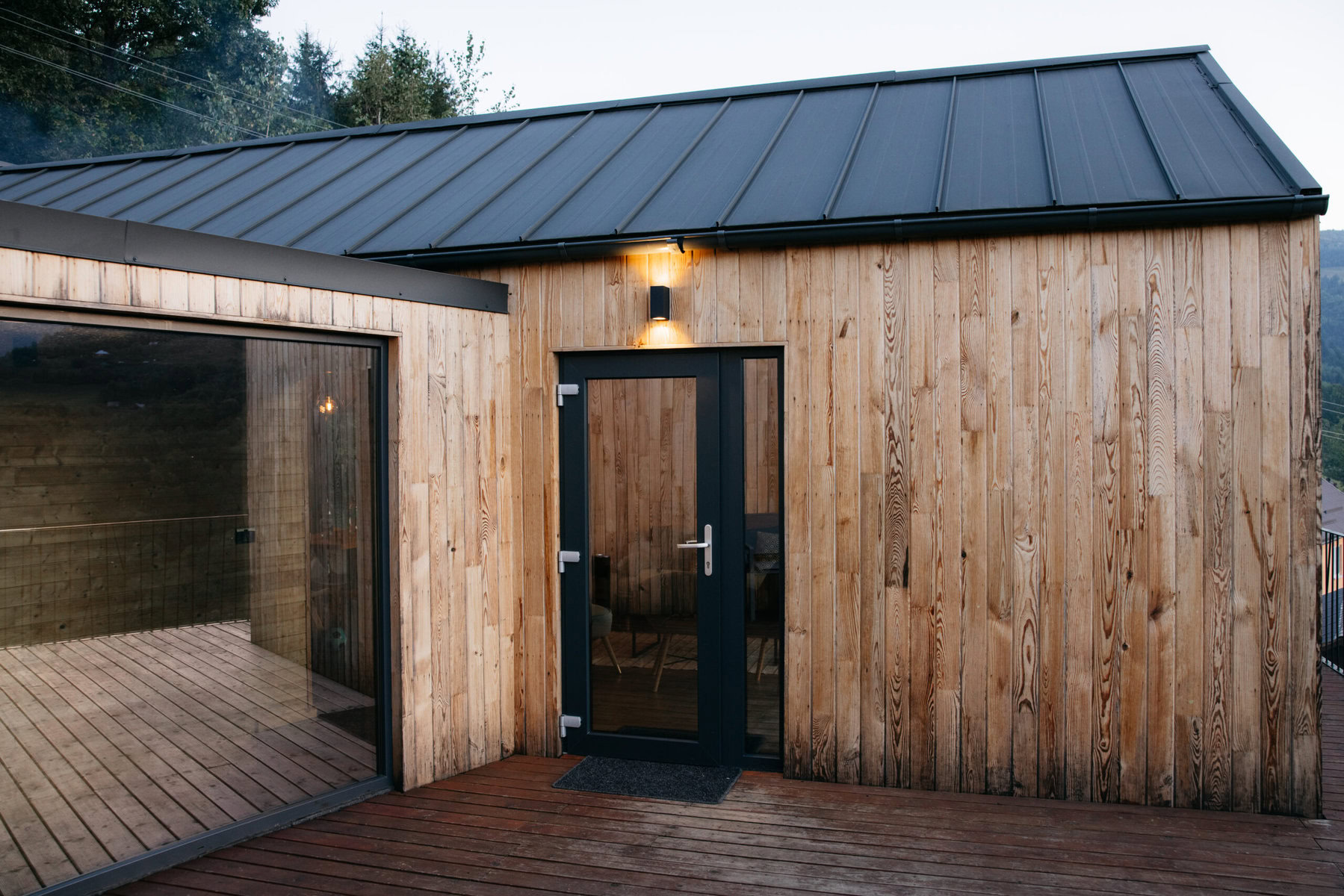 Modern wooden cabin with dark roof and glass door on a deck.