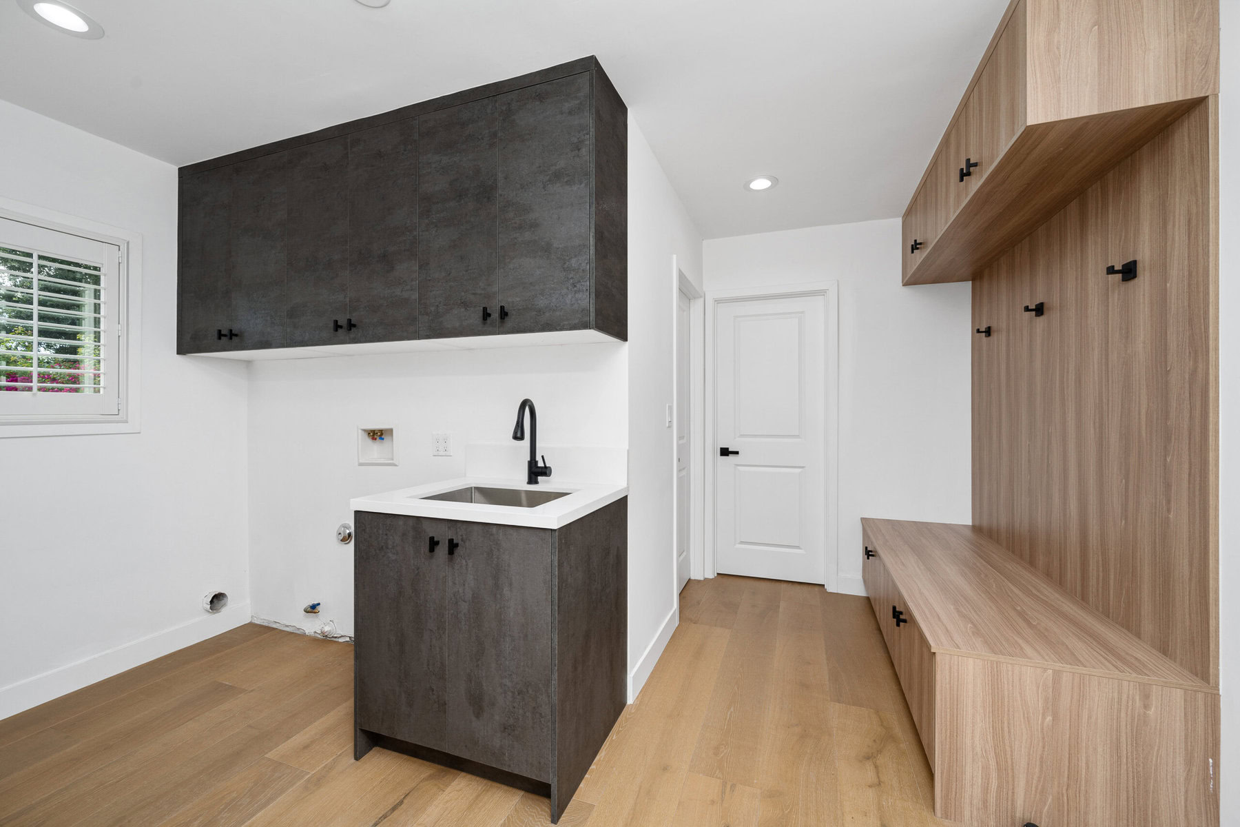 Modern laundry room with dark gray cabinets, a sink, and light wood storage.