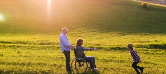 Family enjoying outdoor activity in a green field with wheelchair.
