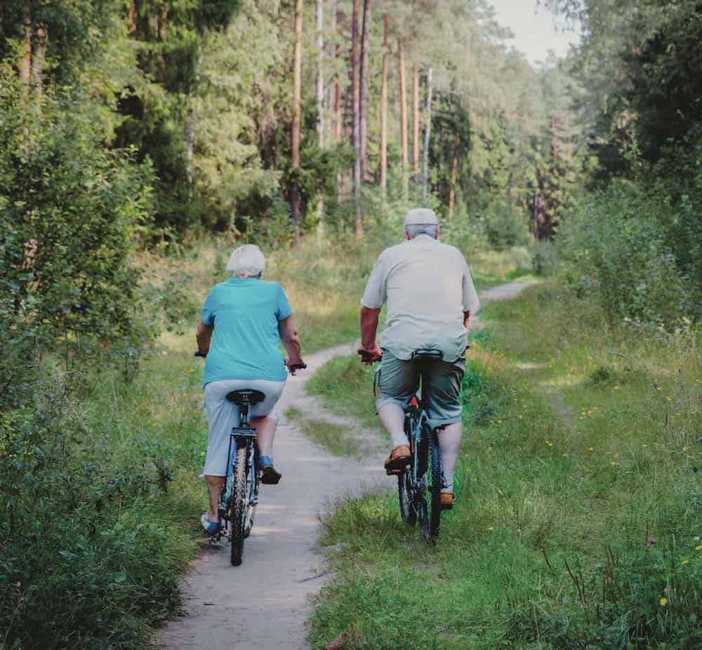 Two seniors cycling on a forest trail for health and recreation.